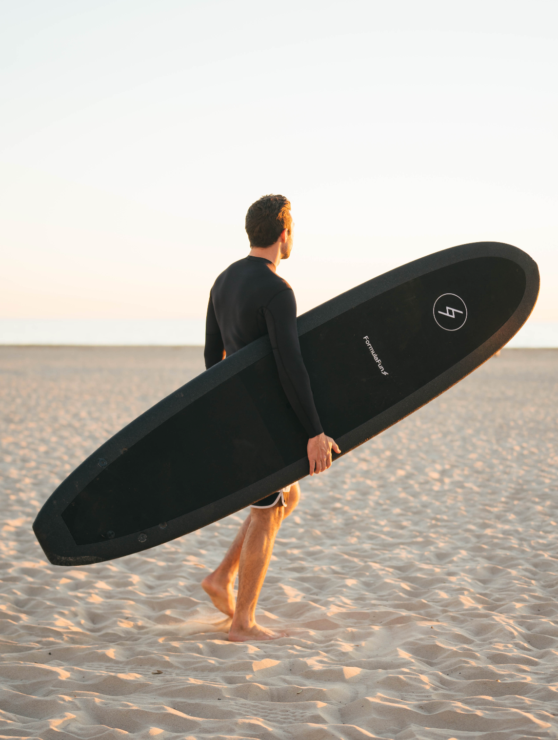 A man on a beach with a black 7 foot 10 inch Formula Fun Foamies DOHO surfboard