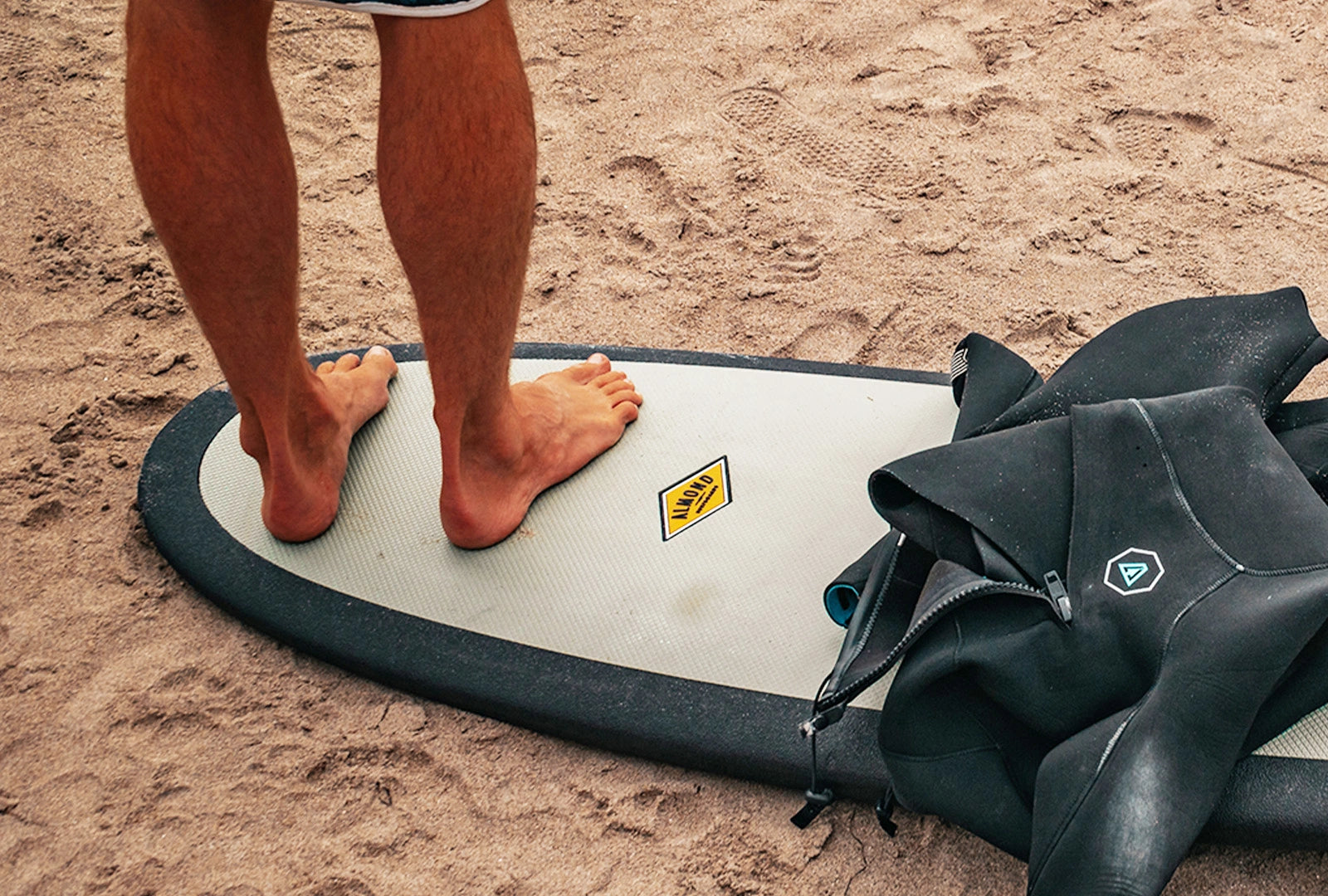 A man standing on an Almond Surfboard in the sand in Newport Beach