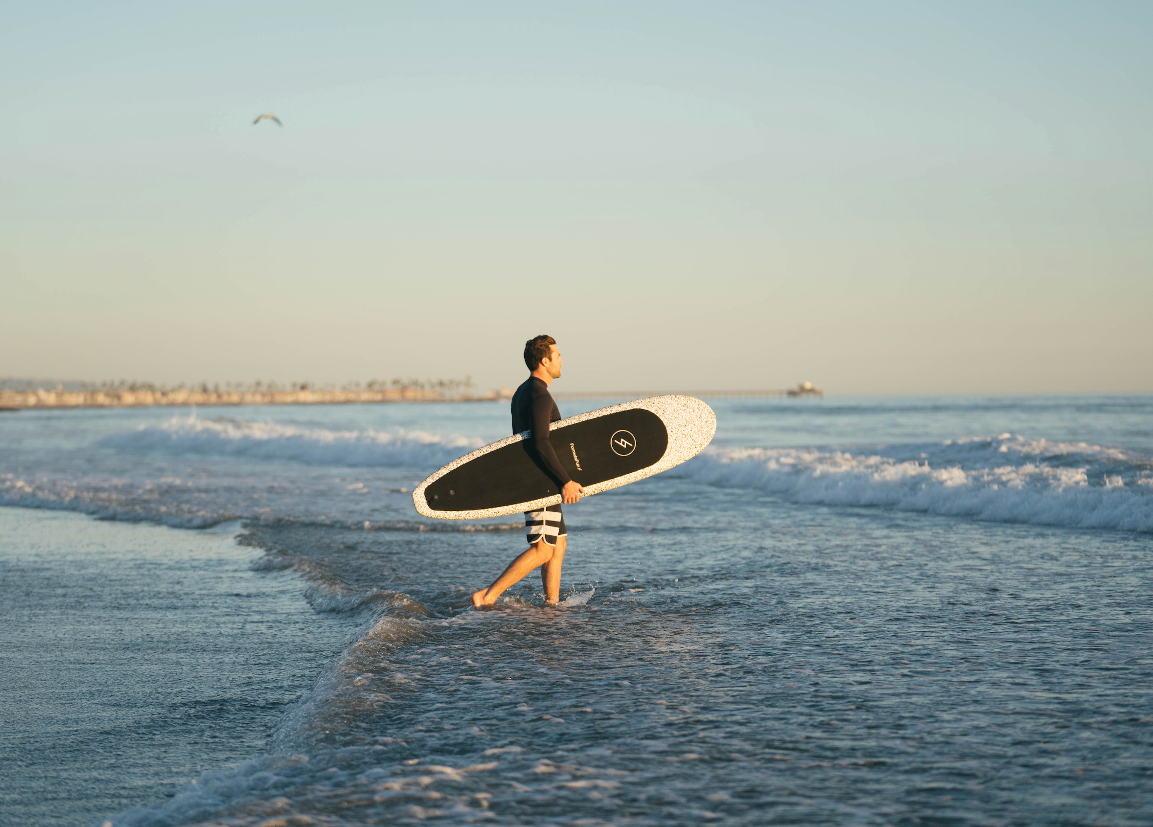 Man entering the water on a beach in a wetsuit with a speckled 6 foot 4 inch Formula Fun Foamies Zipper surfboard