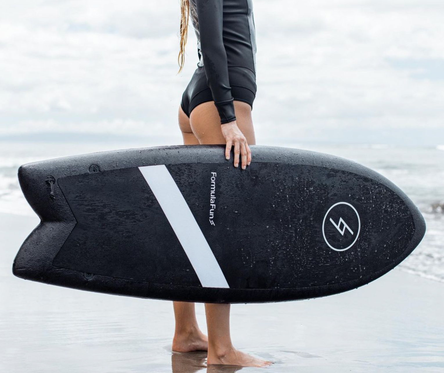 A girl at a beach holding 5 foot 3 inch Formula Fun Foamies Twinnie surfboard