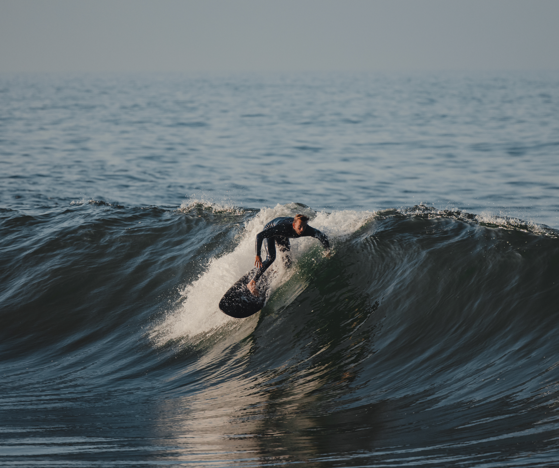 A man surfing a wave on a black 5 foot 4 inch Almond surfboard