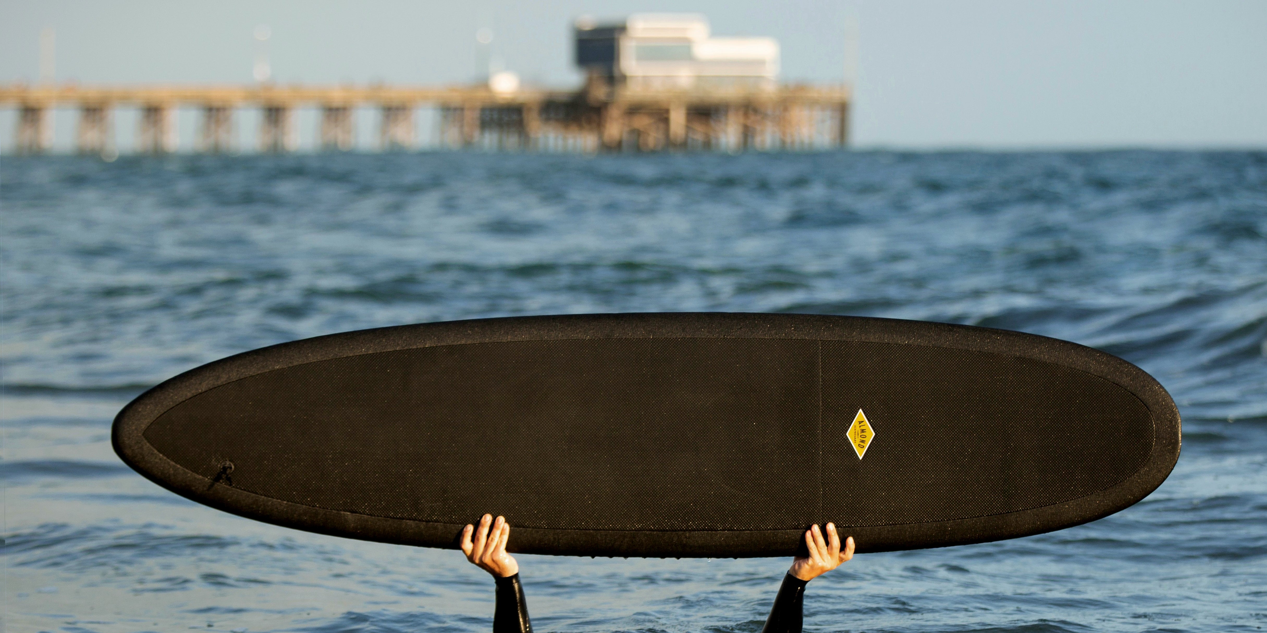 Person in the water holding up a black 8 foot Almond Joy surfboard
