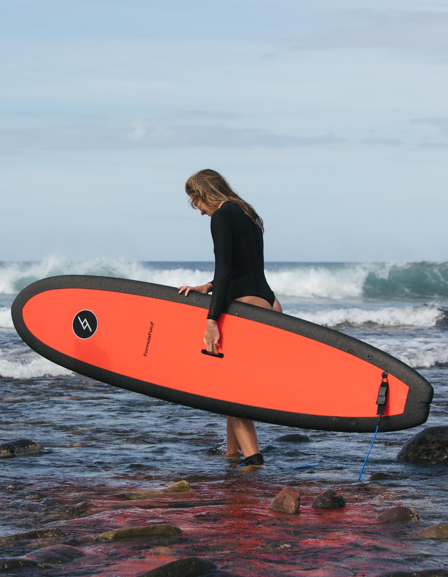 Woman entering the ocean with an orange 7 foot 10 inch Formula Fun Foamies DOHO surfboard