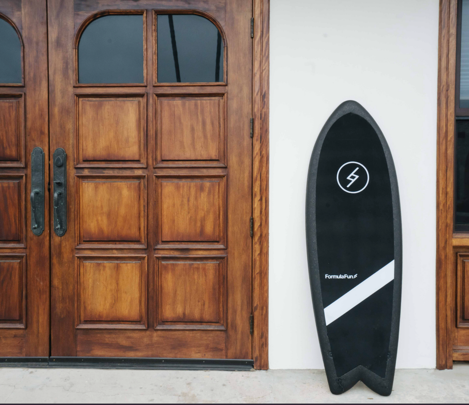 A black 5 foot 3 inch Formula Fun Foamies Twinnie surfboard leaning up against a house