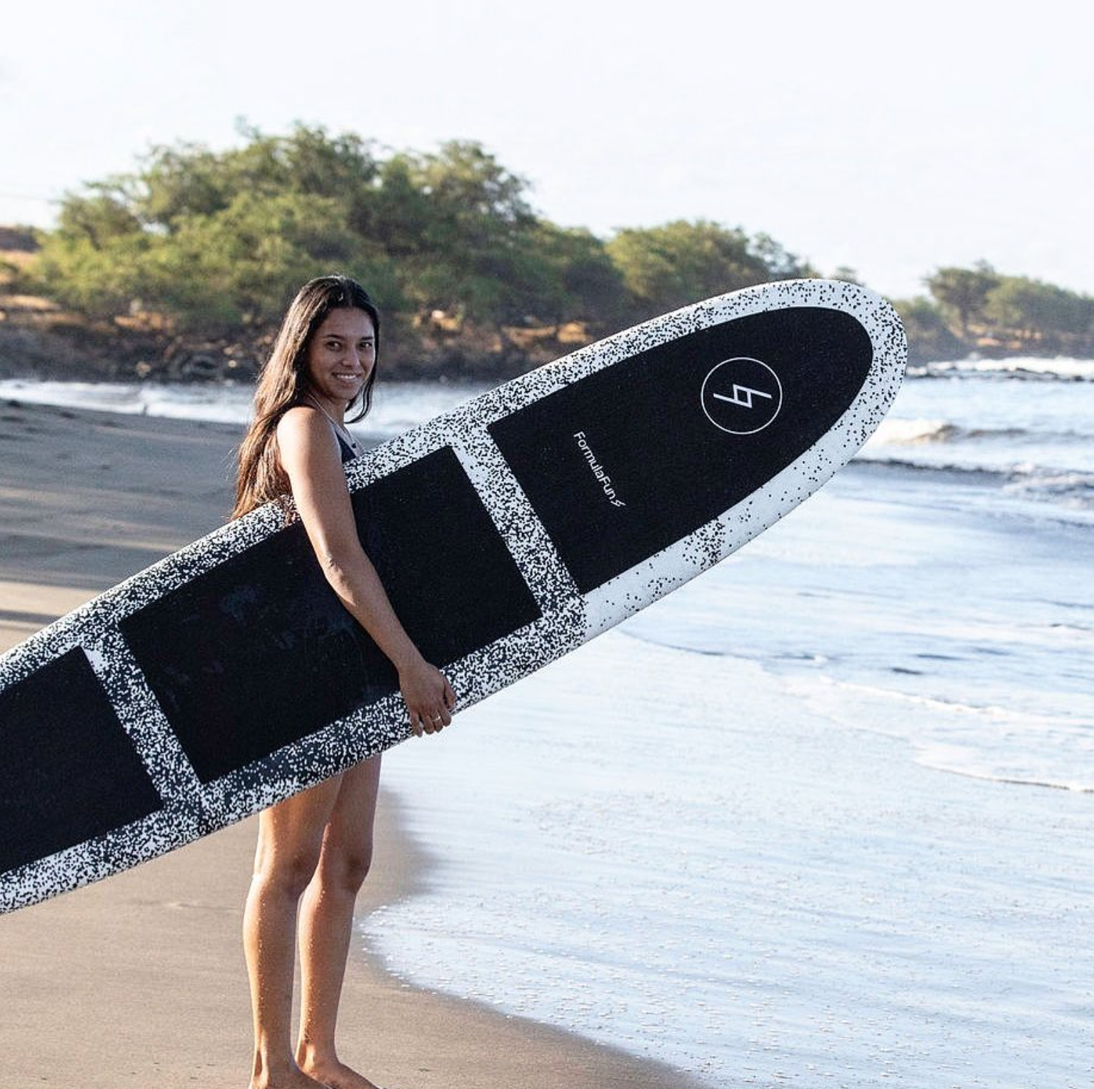 A woman on a beach with a speckled Formula Fun Foamies surfboard