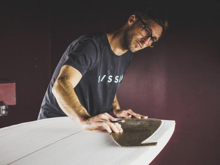 A man putting the finishing touches on a white surfboard