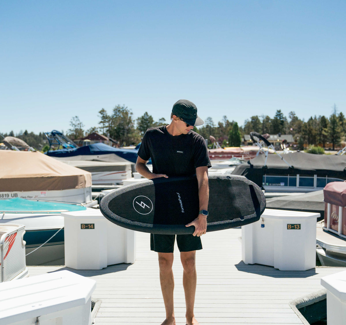 Man holding a black Formula Fun 4'8" Rubicon wakesurf board on a boat dock