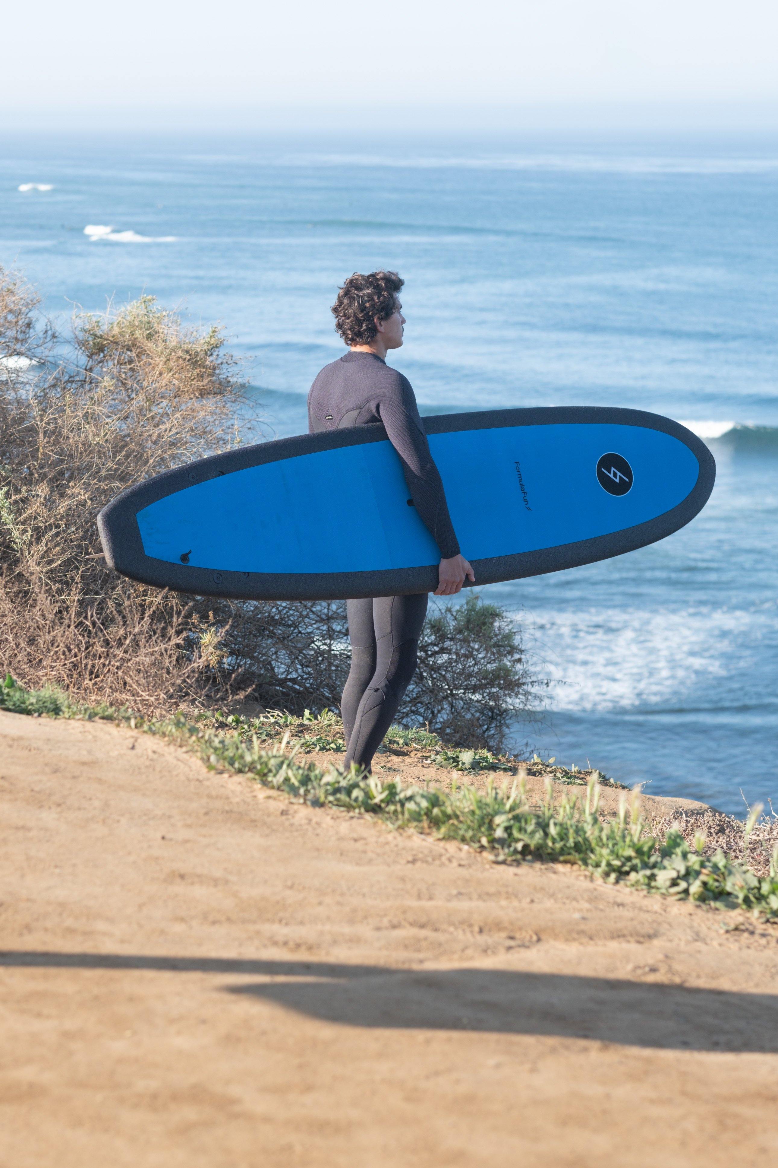 A man on a beach looking at the ocean with a blue 7 foot 10 inch Formula Fun Foamies DOHO surfboard