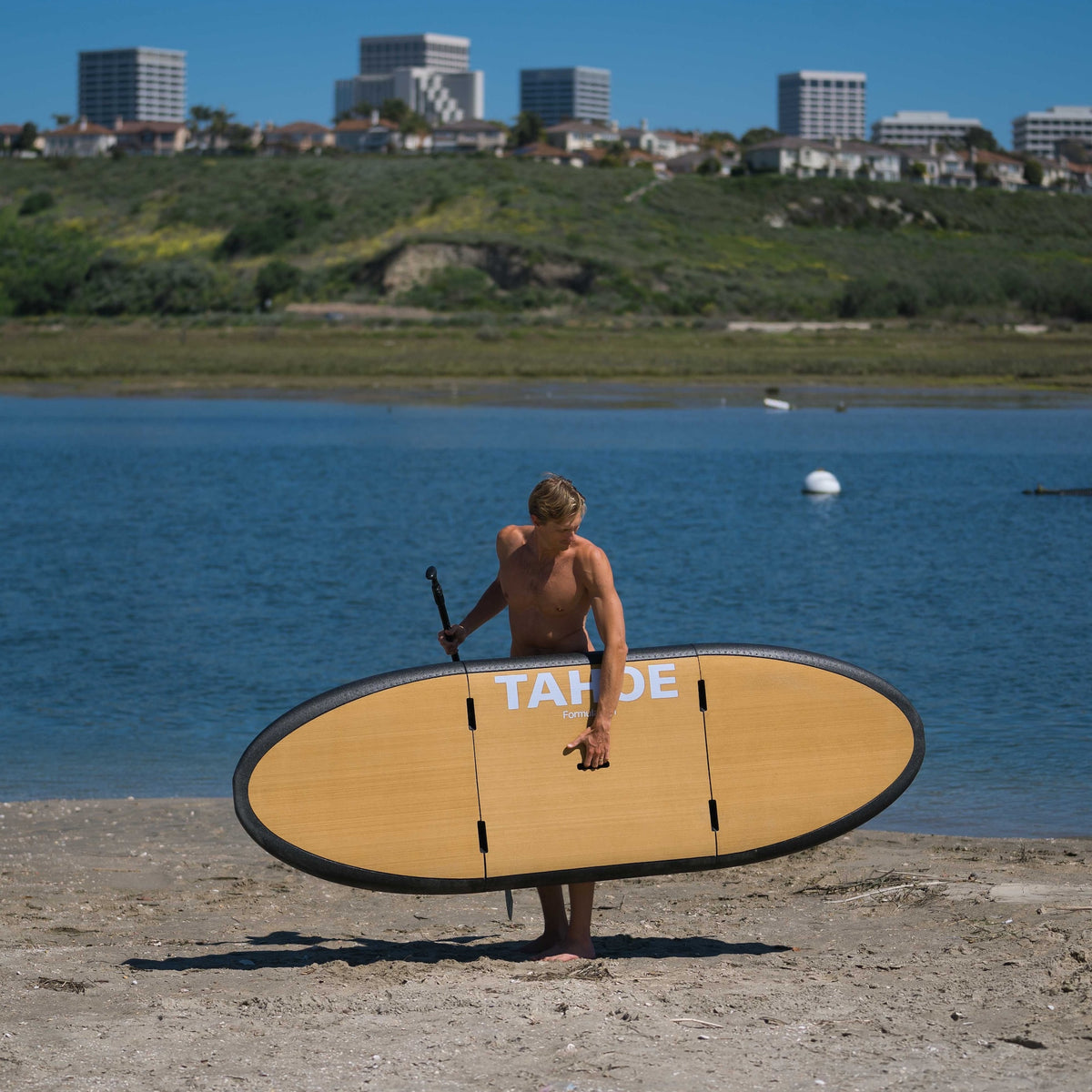 Paddler carrying the Dune Formula Fun Tahoe three-piece SUP beside the water