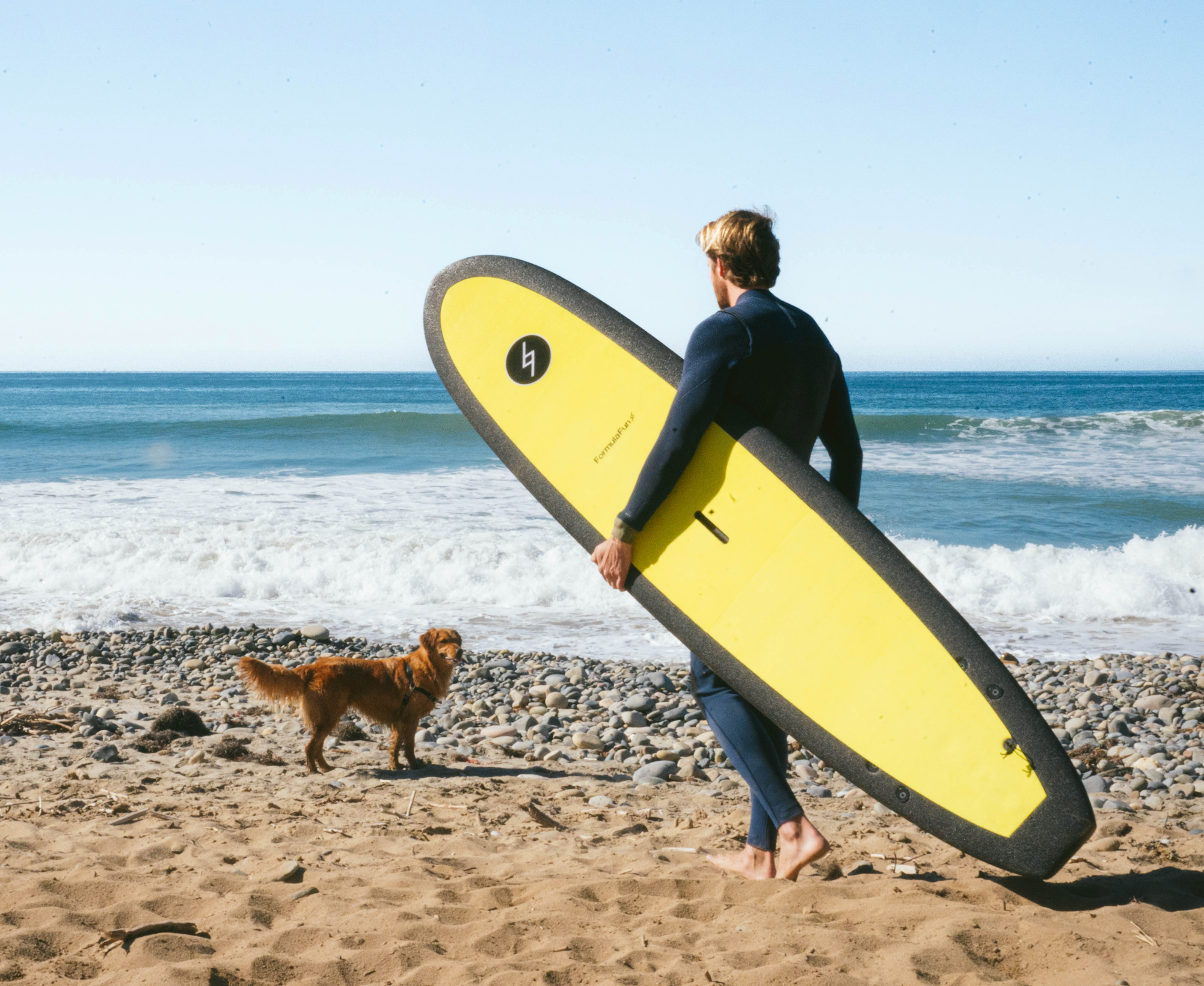 A man and a dog on a beach with a yellow 7 foot 10 inch Formula Fun Foamies DOHO surfboard