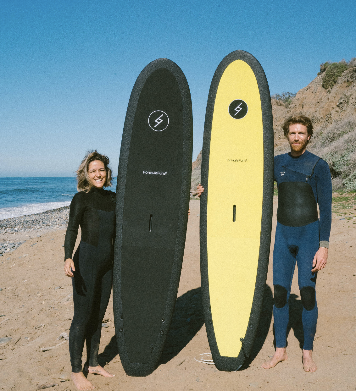 Man and woman on a beach in wetsuits with a black and a yellow 7 foot 10 inch Formula Fun Foamies DOHO surfboard