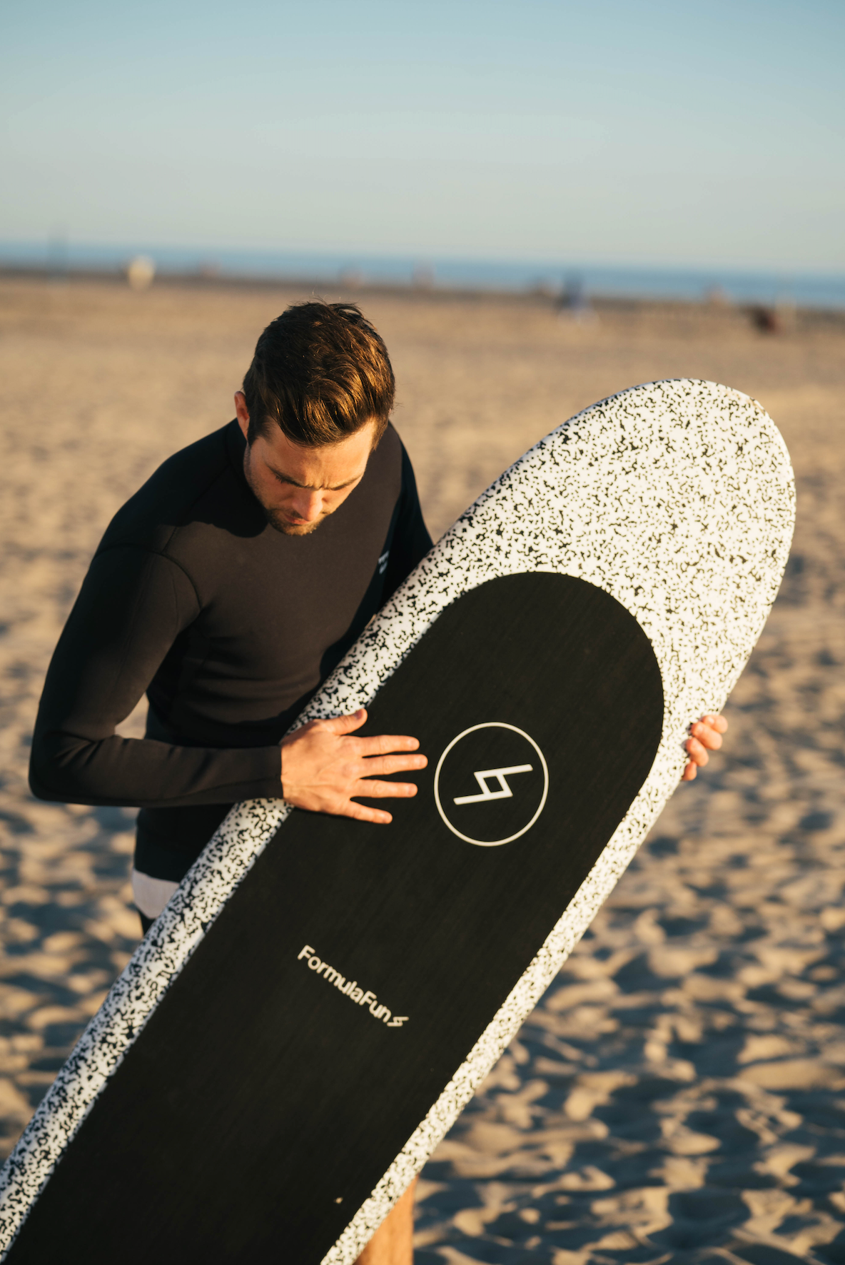 Man on a beach in a wetsuit with a speckled 6 foot 4 inch Formula Fun Foamies Zipper surfboard