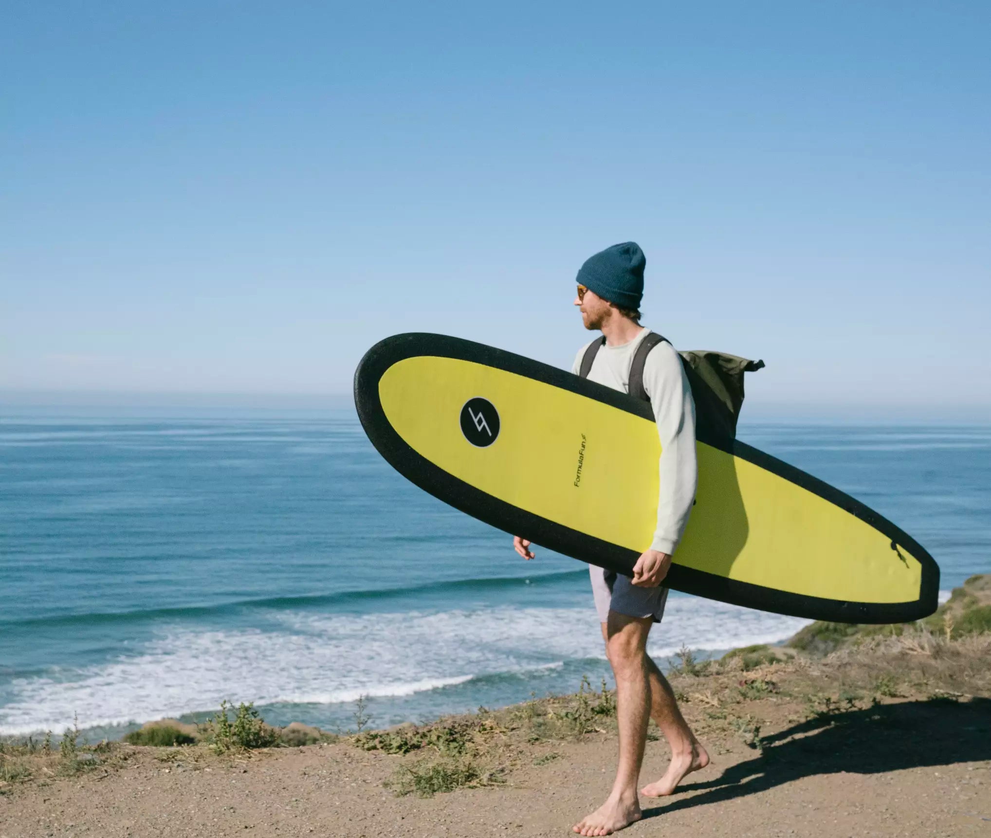 a man holding a yellow 7 foot 10 inch Formula Fun Foamies DOHO board walking on a cliff near the beach