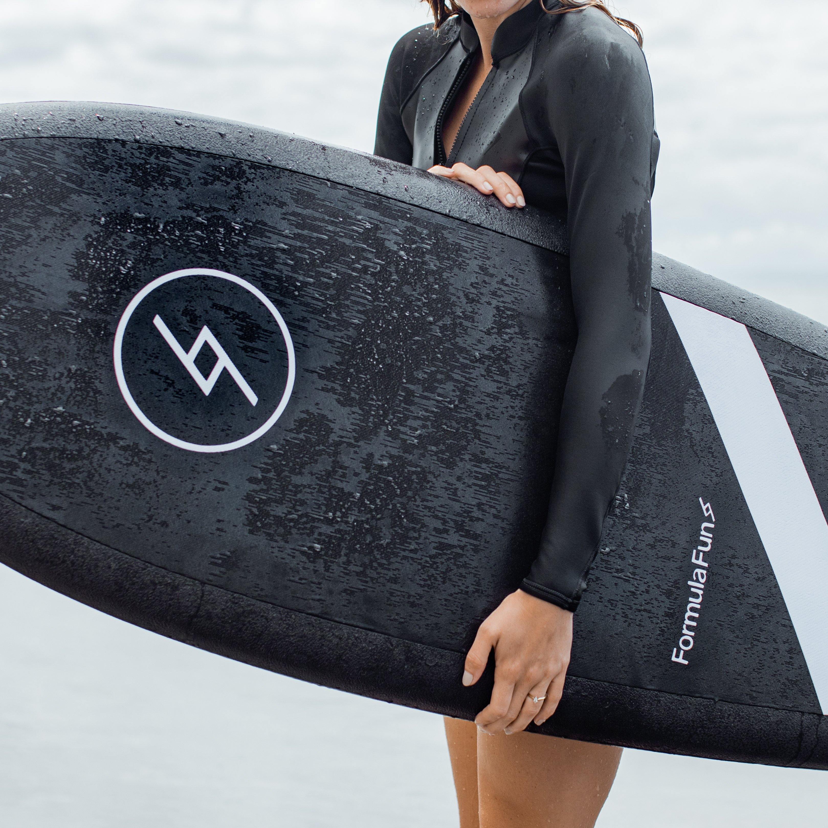 A girl at a beach holding 5 foot 3 inch Formula Fun Foamies Twinnie surfboard