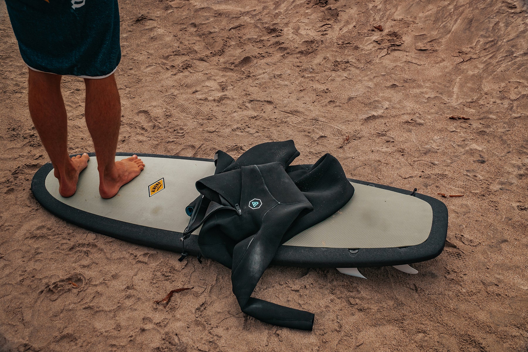 Man standing on a 5 foot 4 inch Almond Secret Menu surfboard next to a wetsuit