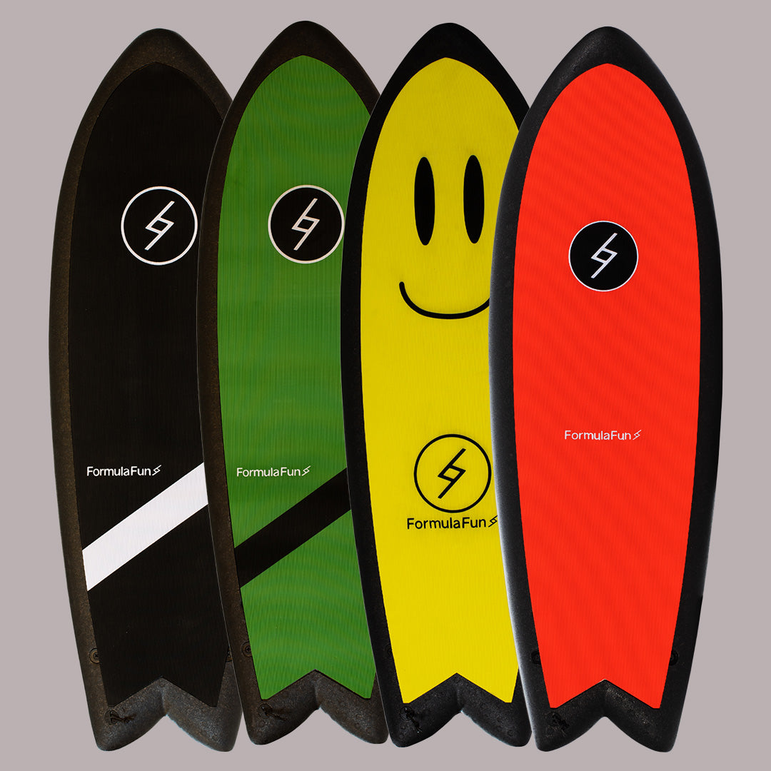 A yellow, a green, a red and a black 5 foot 3 inch Formula Fun Foamies Twinnie surfboard on a grey background