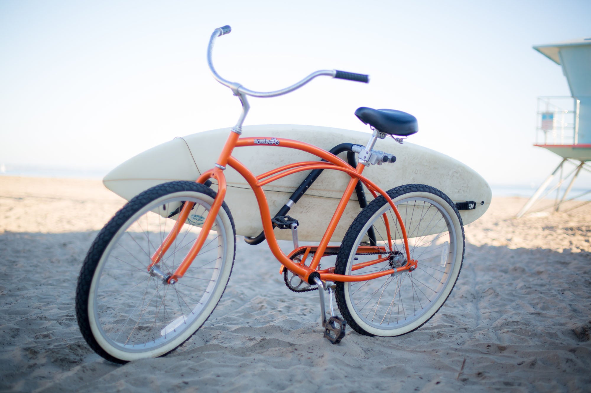 An orange bike on a beach with an MBB shortboard rack carrying a shortboard