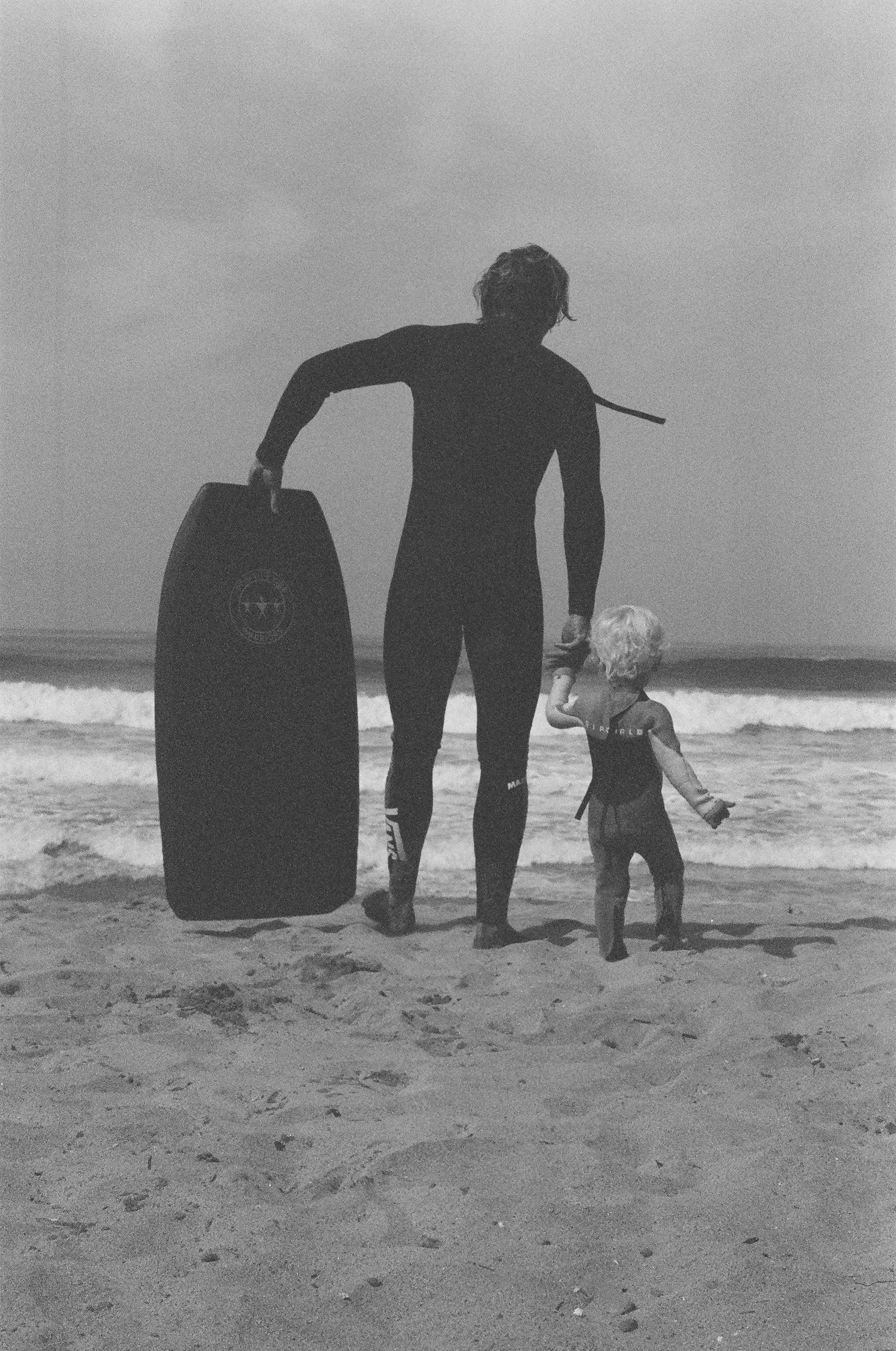 A man on a beach holding a Positive Vibe Warriors Slide Boogie Board in his left hand and a child in his right hand