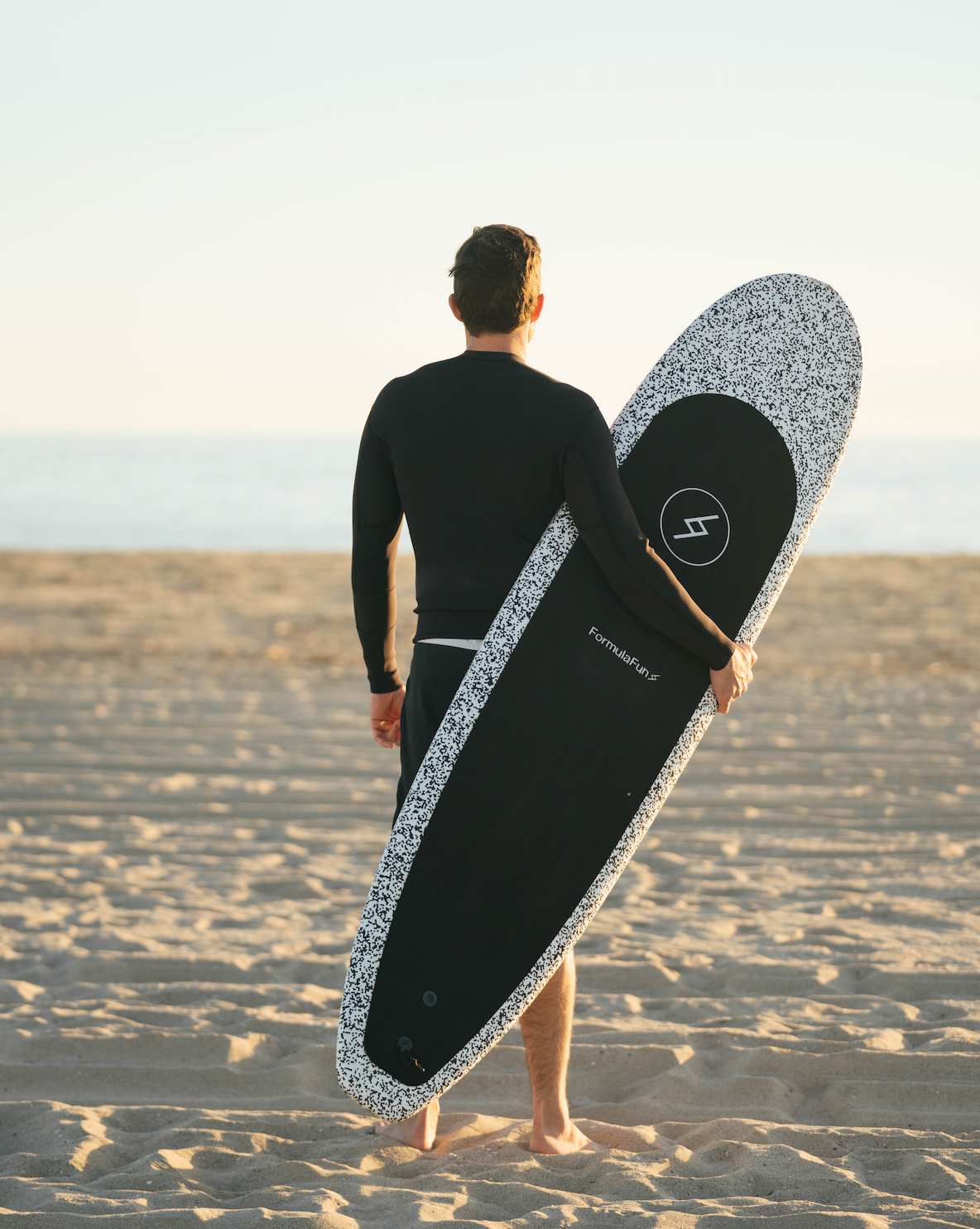Man on a beach in a wetsuit with a speckled 6 foot 4 inch Formula Fun Foamies Zipper surfboard