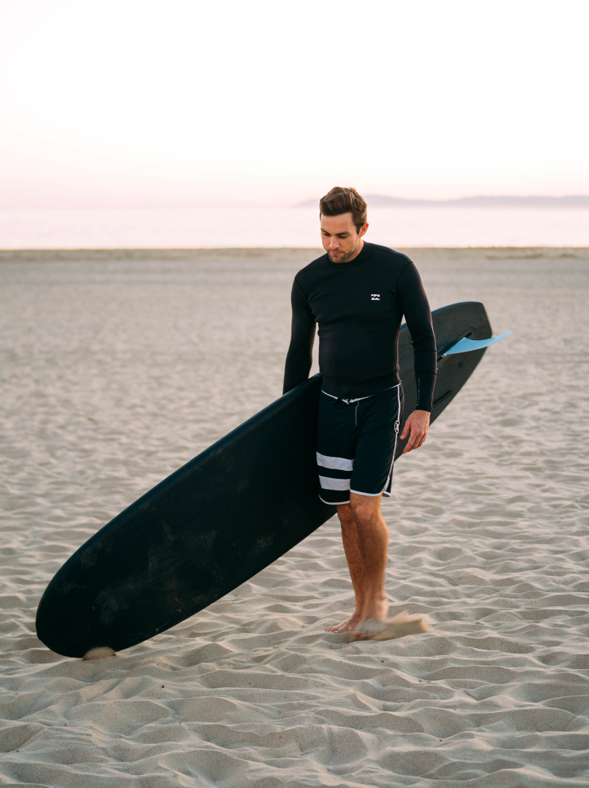 A man on a beach with a black 7 foot 10 inch Formula Fun Foamies DOHO surfboard