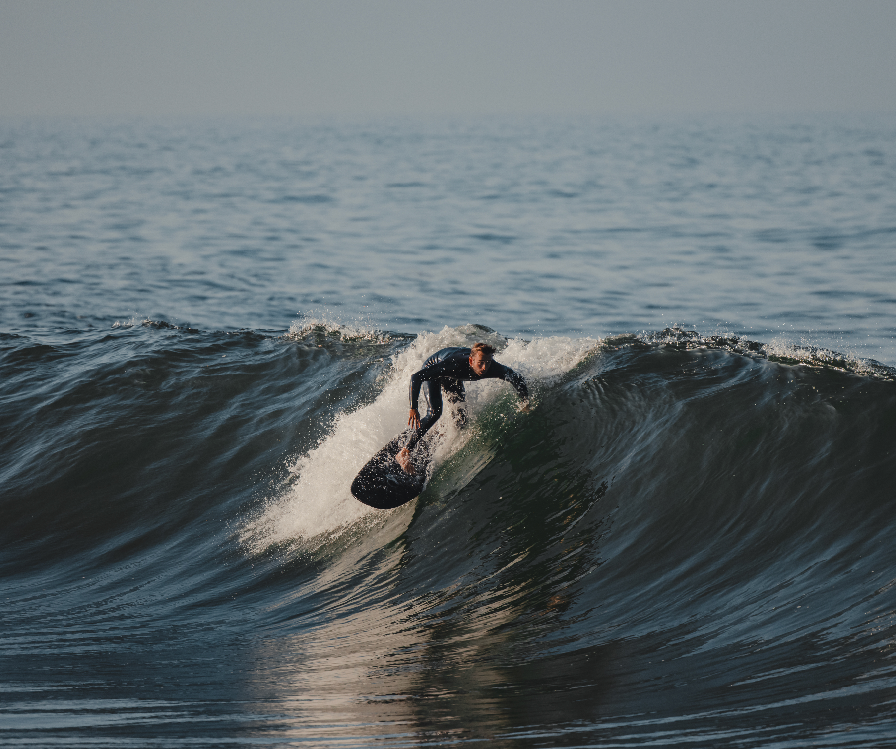 A man surfing a wave on a black 5 foot 4 inch Almond surfboard 