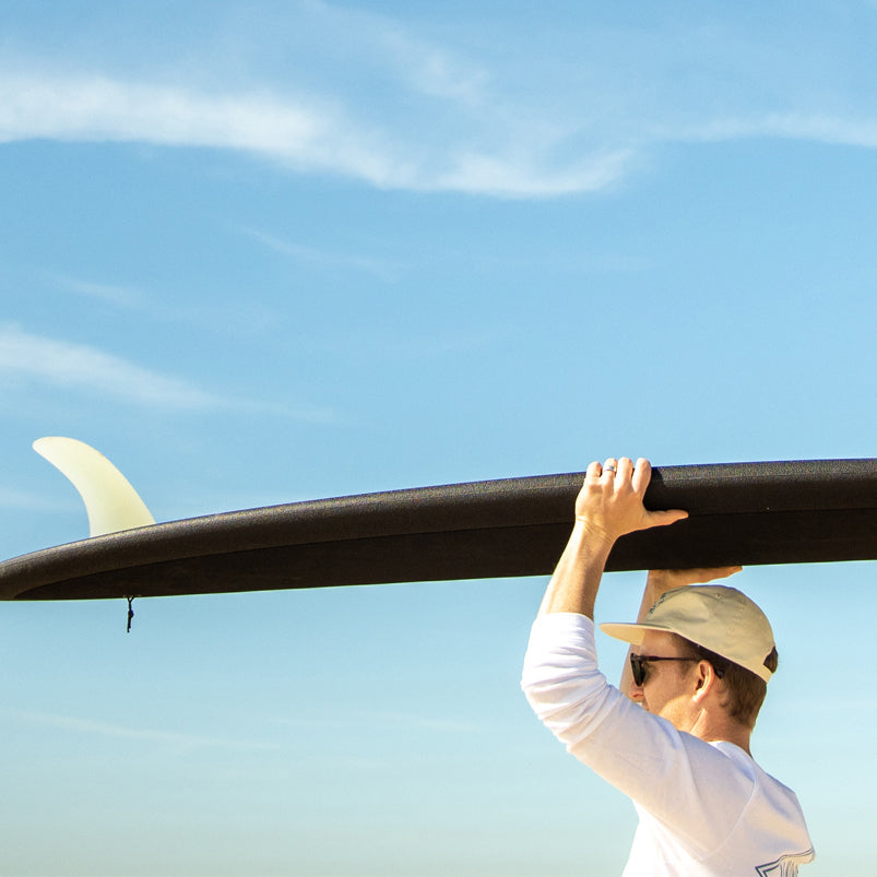 Man carrying a black 8 foot Almond Joy surfboard on top of his head