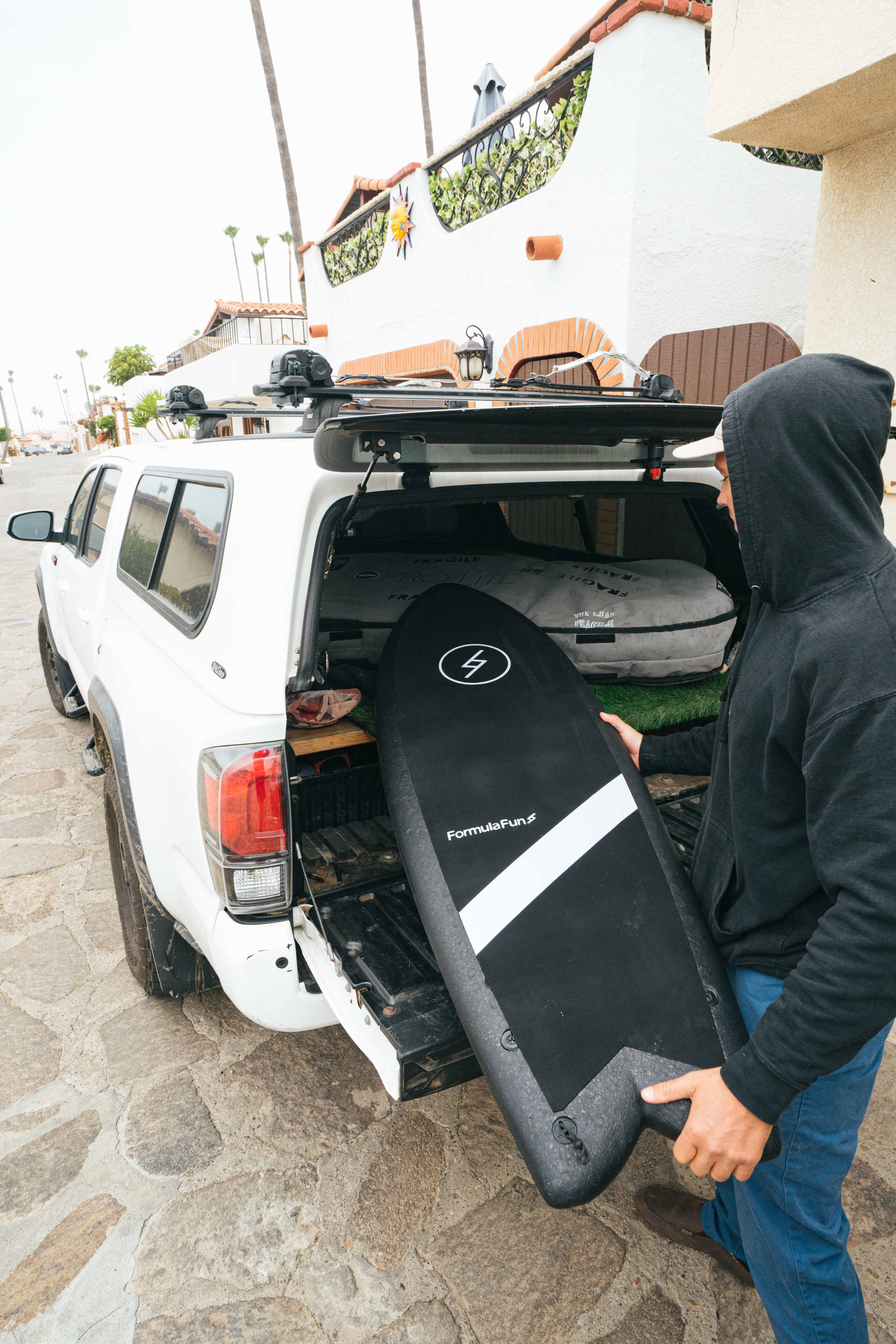 A rider loads a black Formula Fun board into the open back of a truck
